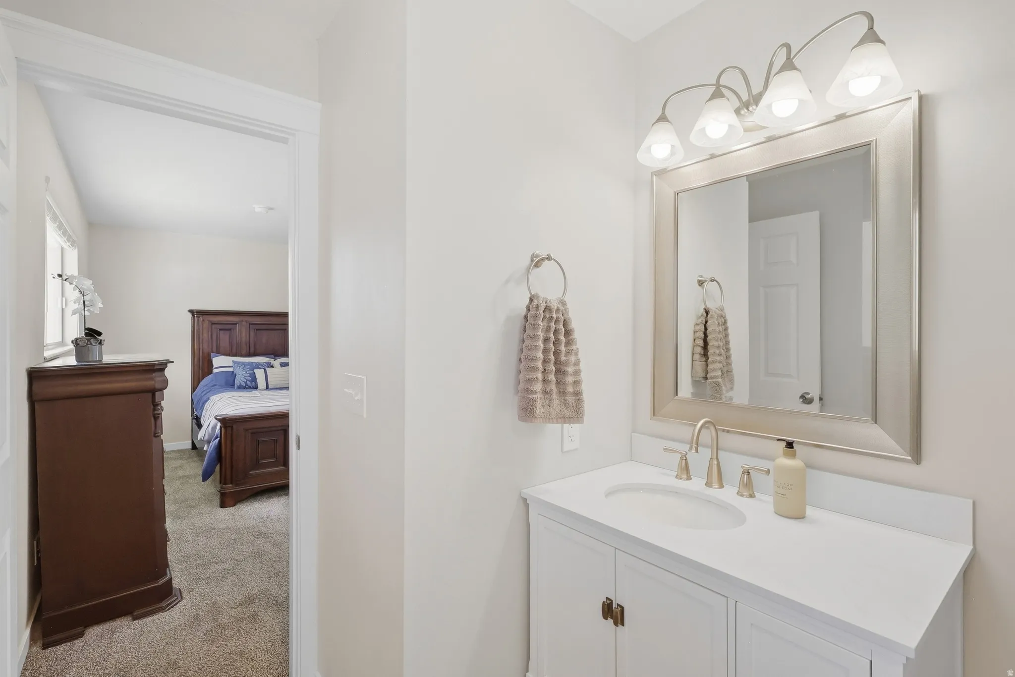 Single-sink vanity with a white countertop, framed mirror, and a four-light fixture