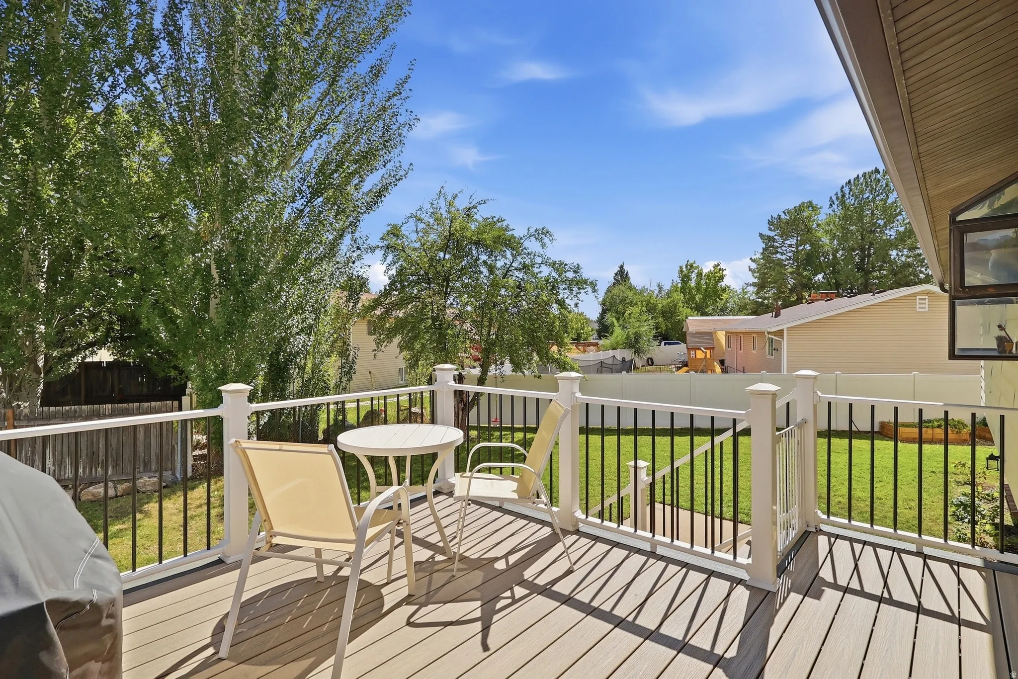 Outdoor deck with composite decking, white railing with black balusters, and a fenced backyard with green lawn