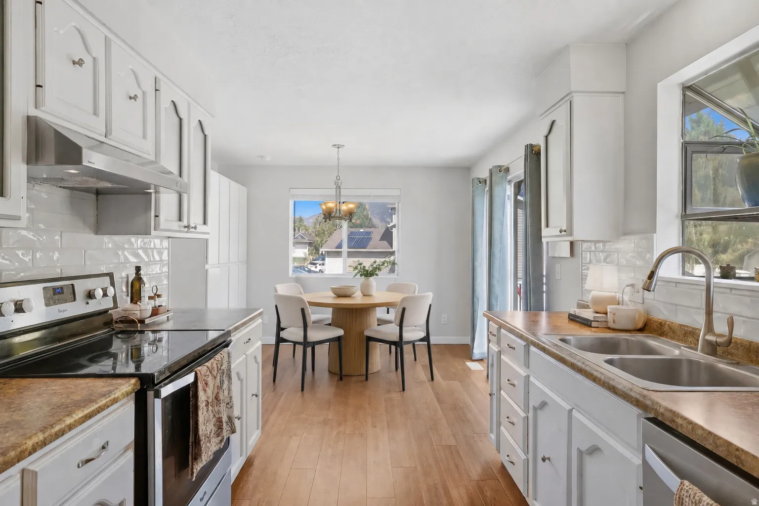 Kitchen featuring white cabinetry, subway tile backsplash, stainless steel appliances, wood-finish flooring, and a double basin sink
