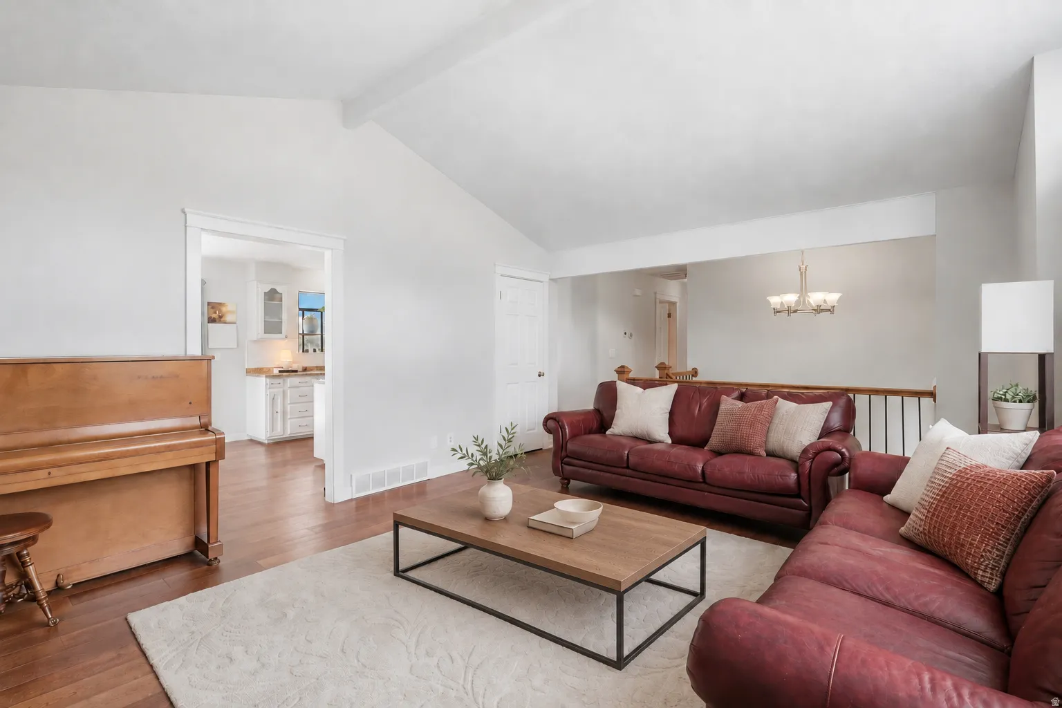 Vaulted ceiling with exposed beam, wood-finish flooring, white wall paint, built-in shelving, and a metal and wood railing