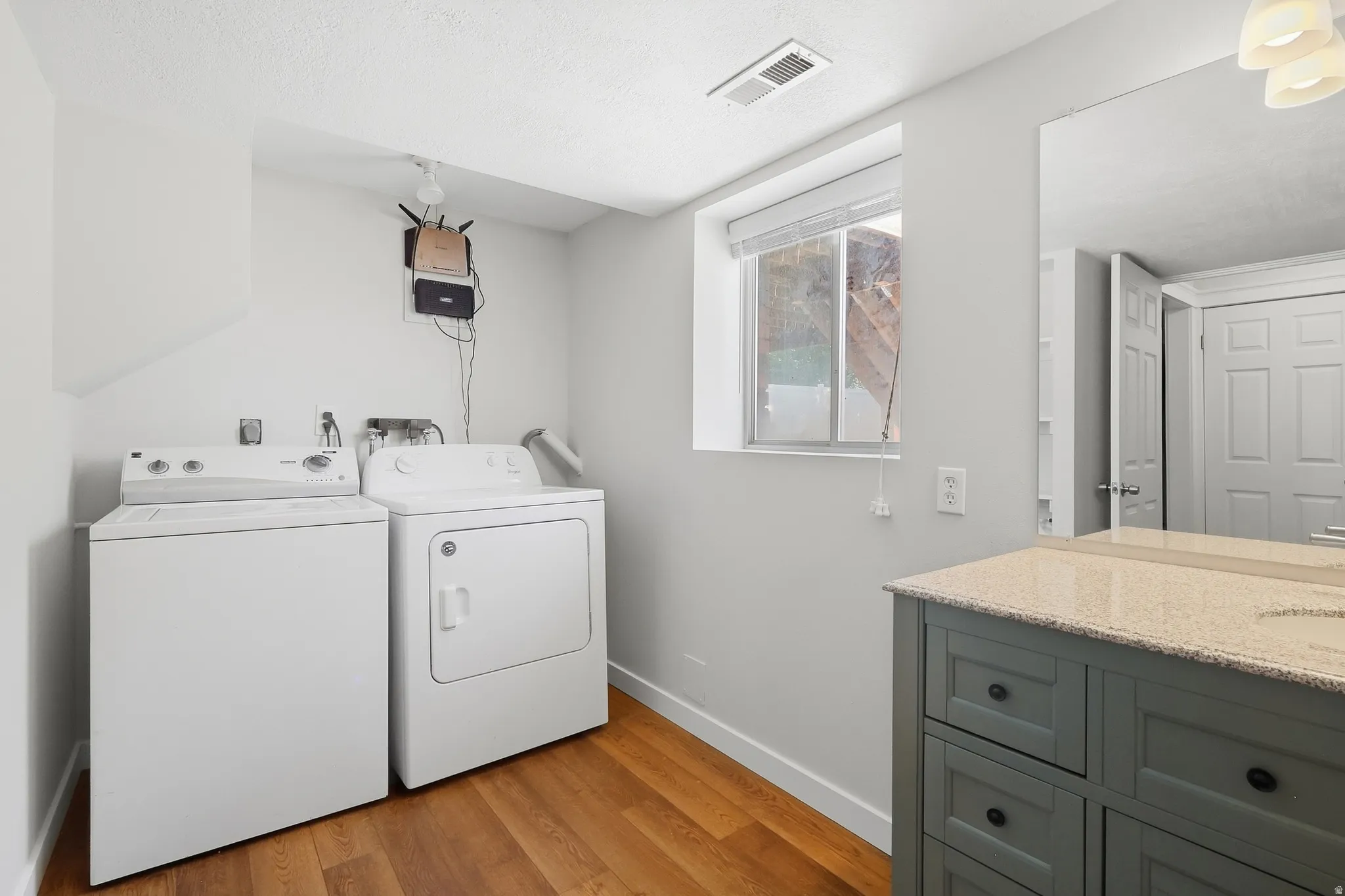 Hardwood flooring, light gray walls, built-in vanity with light-toned countertop, and dual laundry appliances