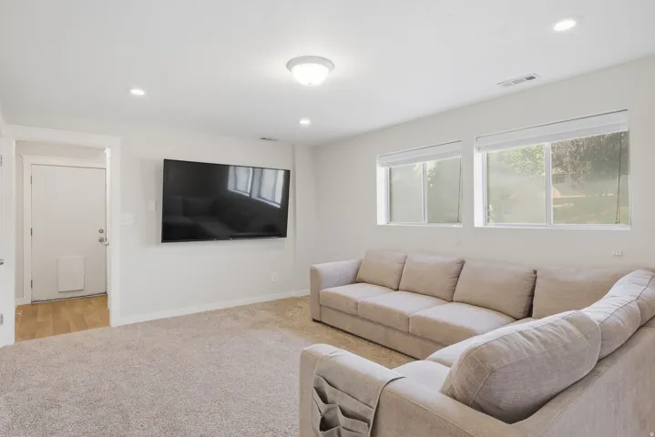 Neutral tone carpeting, dual flush-mounted ceiling lights, recessed lighting, and multiple windows with roller shades