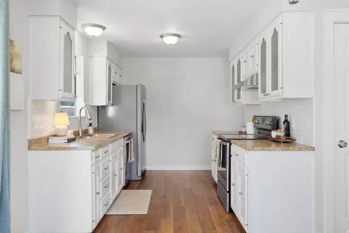 Bright kitchen featuring white cabinetry, wood-finish flooring, a stainless steel refrigerator, stone-look countertops, and a subway tile backsplash