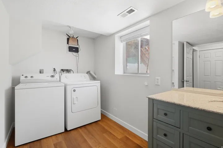 Hardwood flooring, light gray walls, built-in vanity with light-toned countertop, and dual laundry appliances