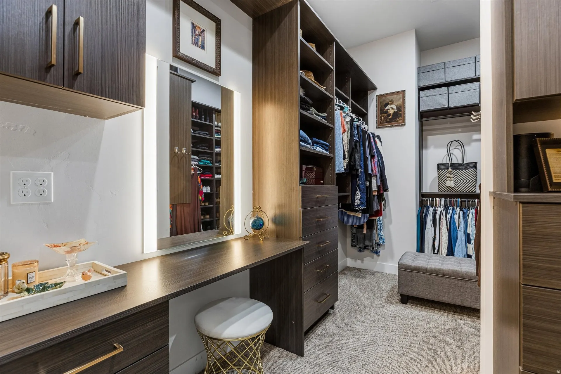 Primary walk-in closet with a lit vanity mirror and built-in cabinetry.