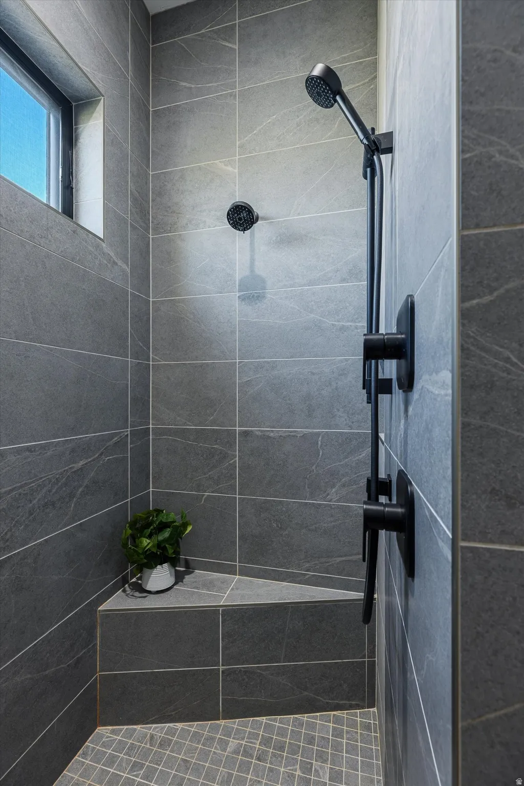 Guest shower detail — custom tile, dual shower heads, vaulted ceiling, and a built-in bench.