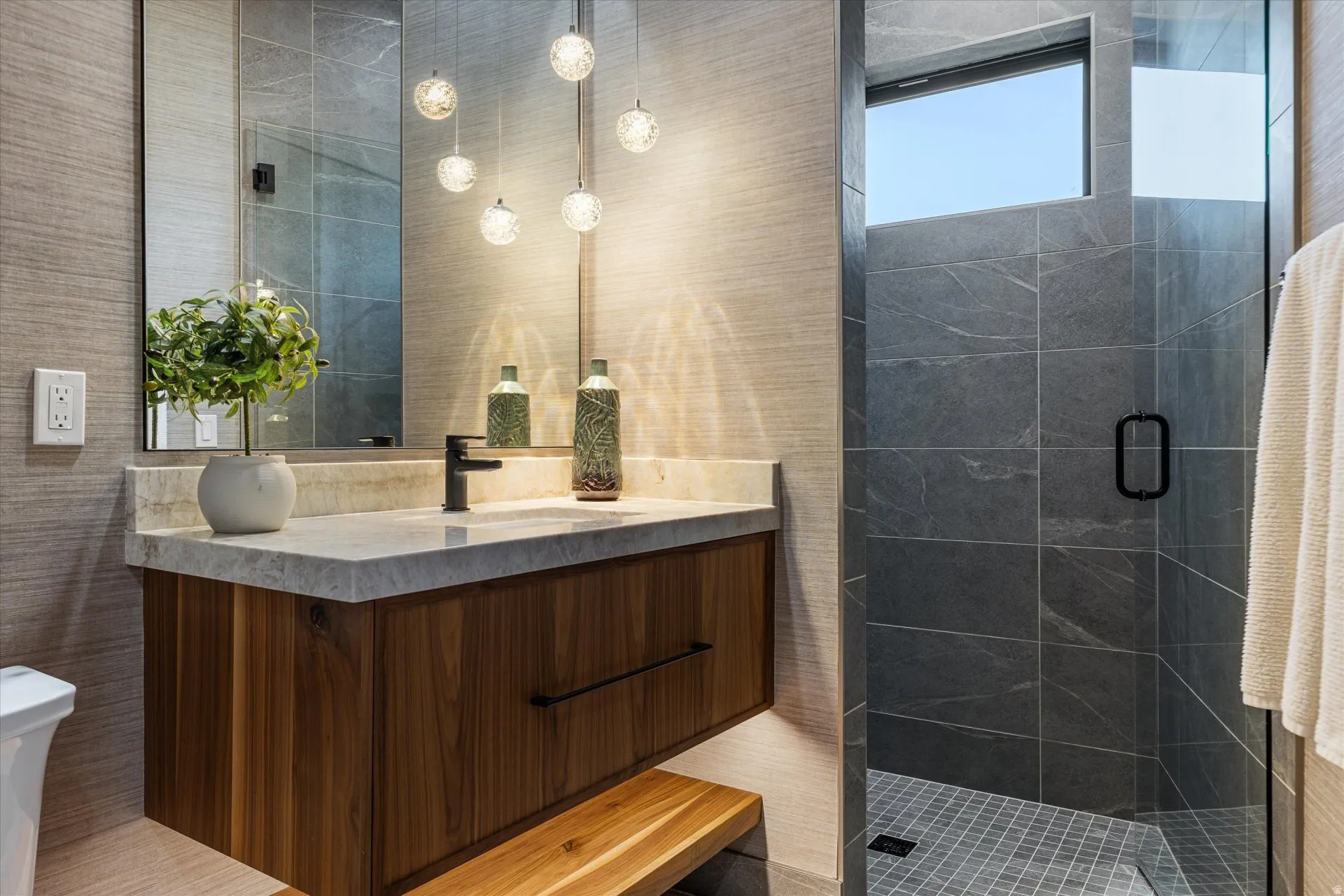 Full bath off the hallway — a floating lit vanity, custom pendant lighting, marble countertop, and a walk-in shower.