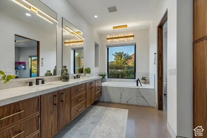 Primary bath soaking tub beneath an alabaster-style chandelier, framed by a picture window looking out at Mt. Kinesava, plus a floating dual vanity.