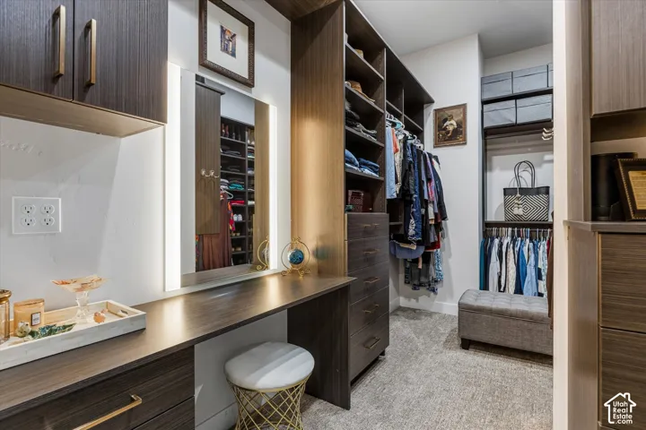 Primary walk-in closet with a lit vanity mirror and built-in cabinetry.