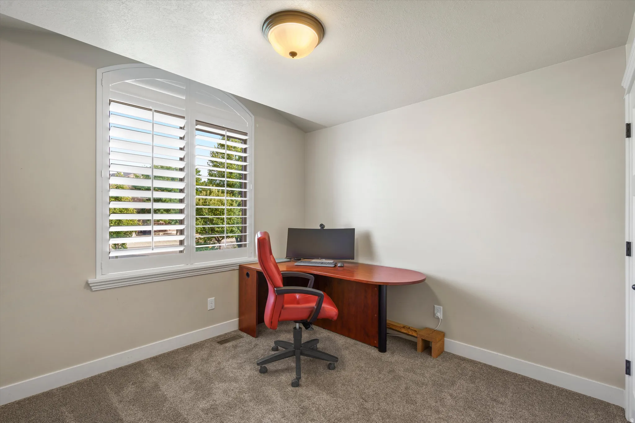 Arched window with white plantation shutters, neutral wall paint, and textured carpeting