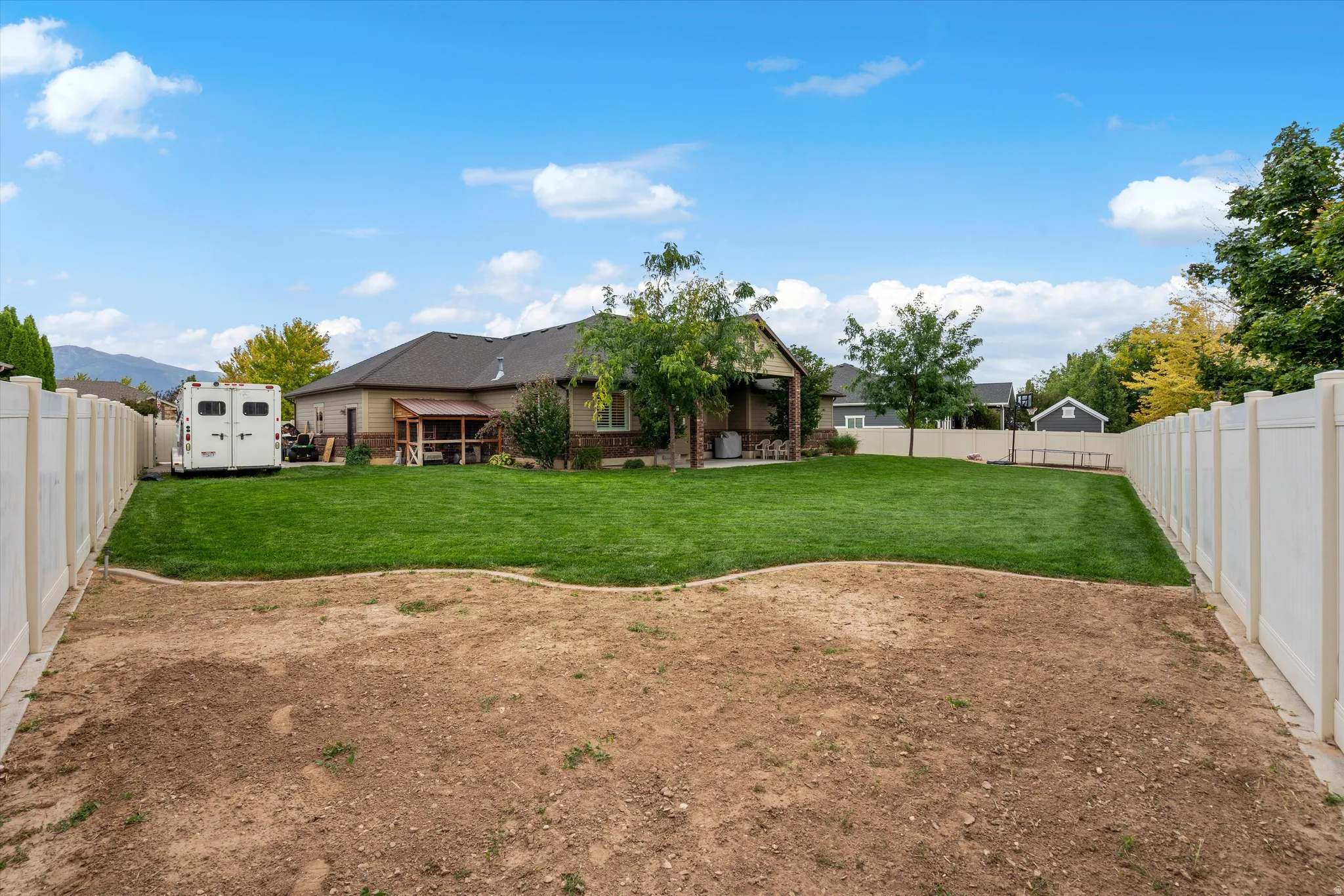 Expansive fenced yard featuring a manicured lawn, established trees, and a covered patio area