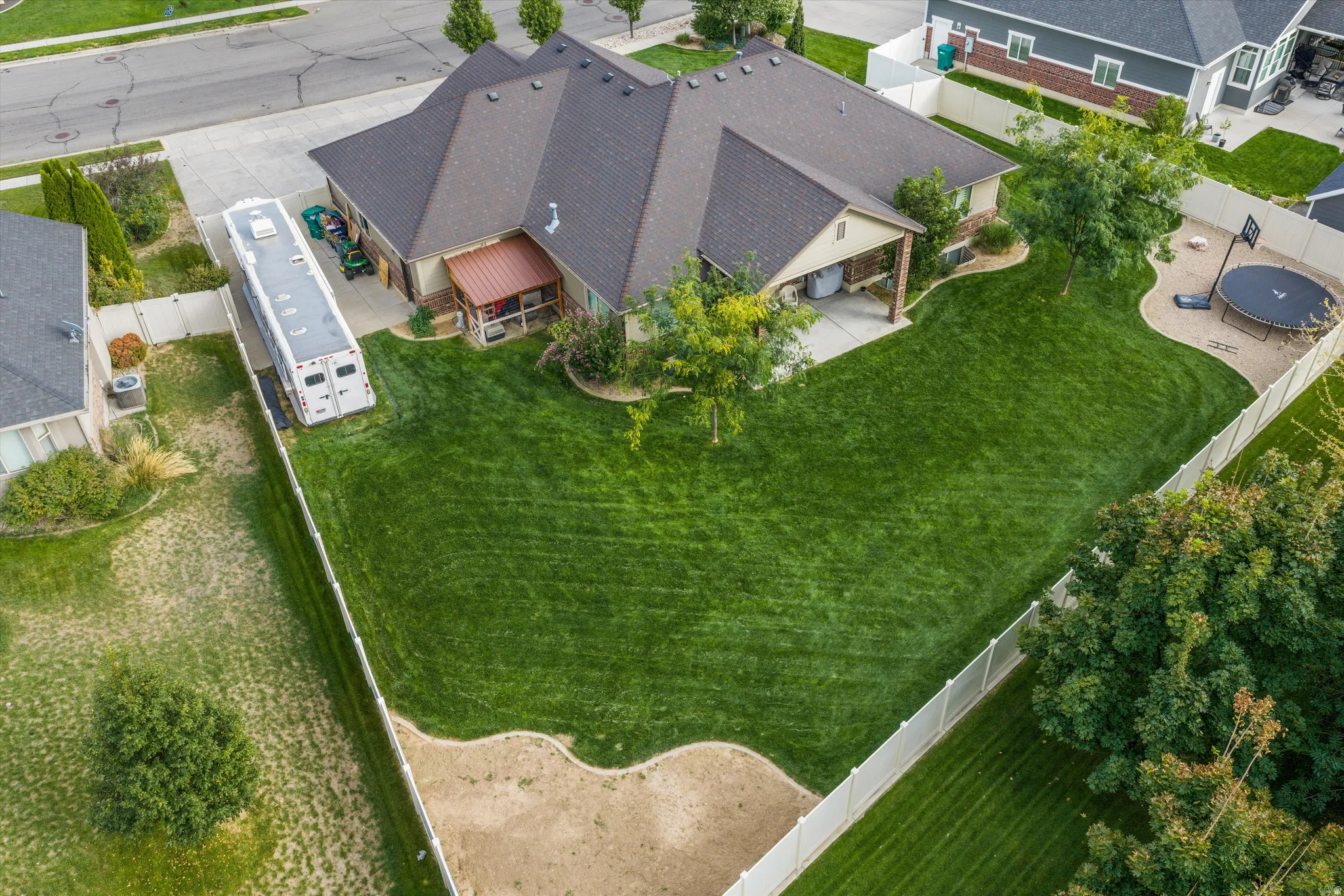 Expansive rear yard featuring a manicured lawn, established trees, covered patio, and perimeter fencing