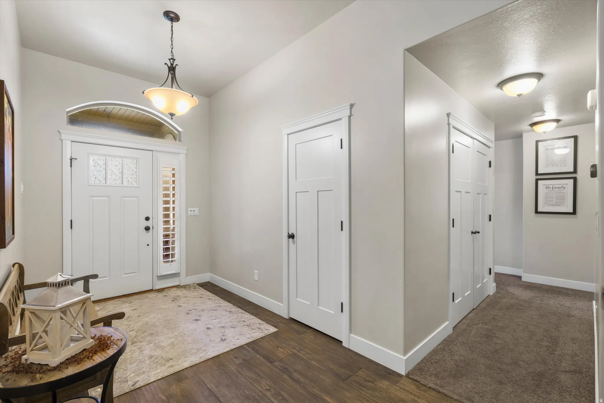 Entryway featuring wood-finish flooring, a decorative pendant light, and a white front door with sidelight and transom window