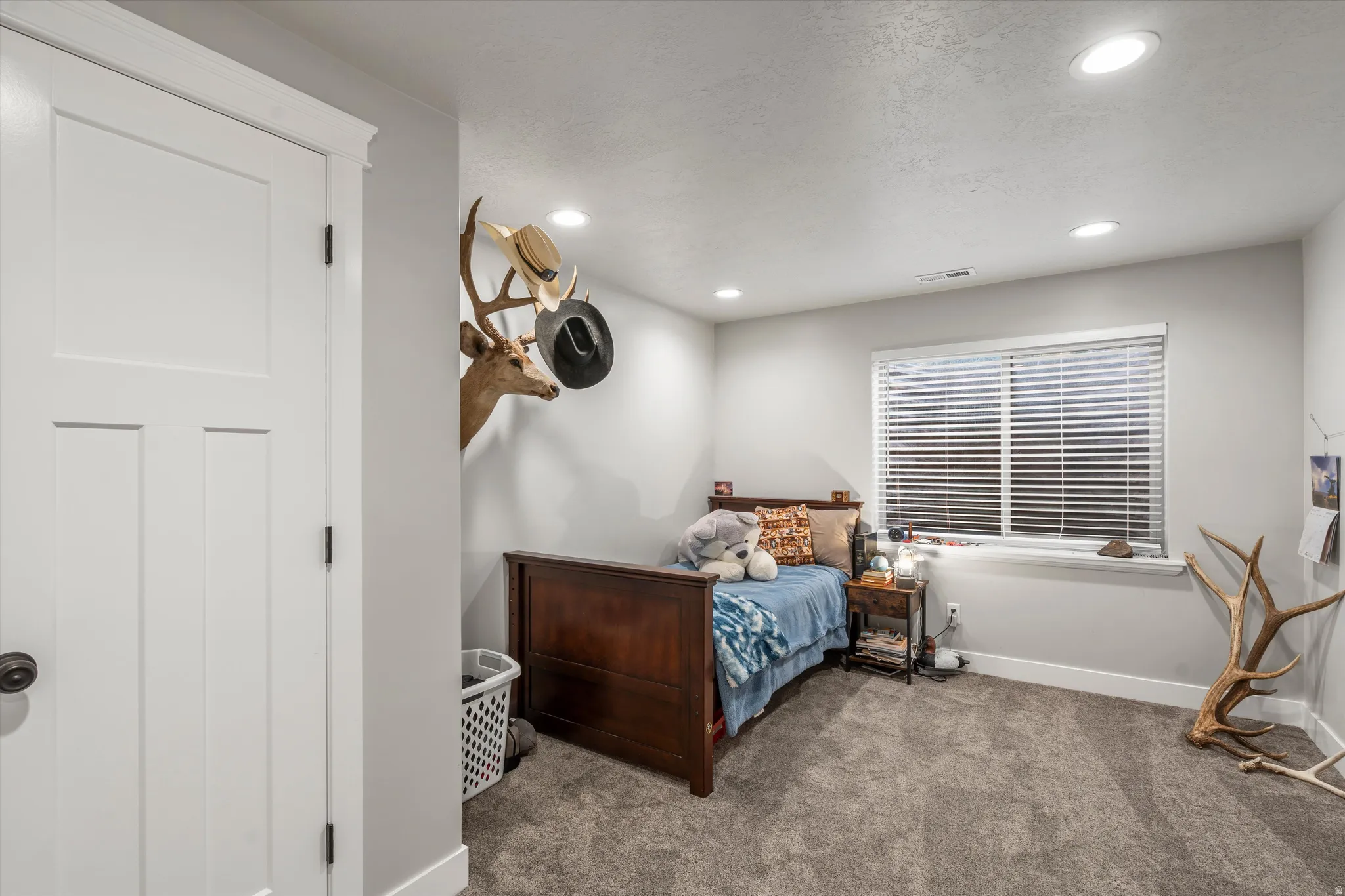 Recessed ceiling lighting, a white paneled door with dark hardware, a window with blinds, and neutral-toned wall paint