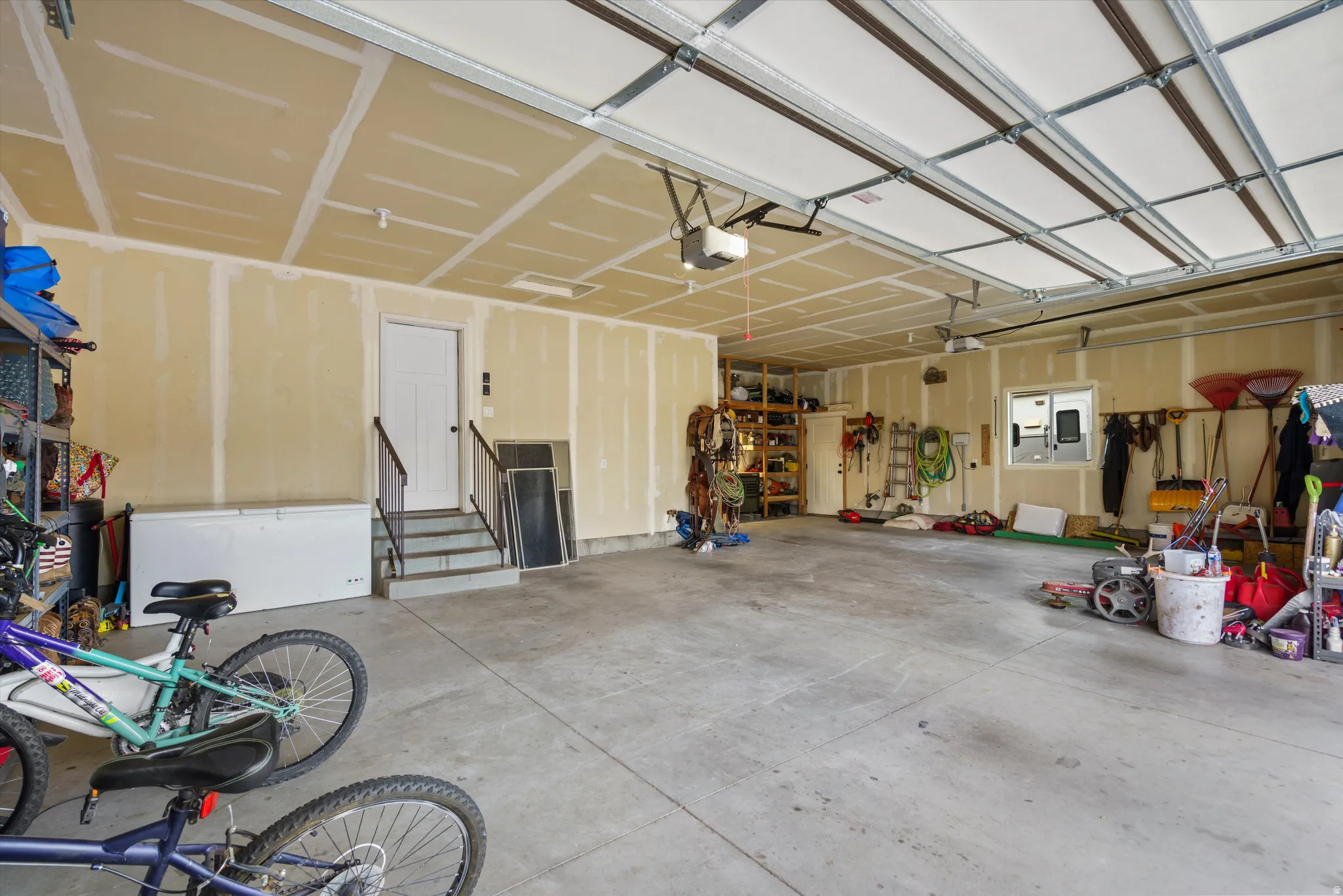 Spacious garage featuring concrete flooring, an overhead garage door, built-in shelving, and a utility door with steps