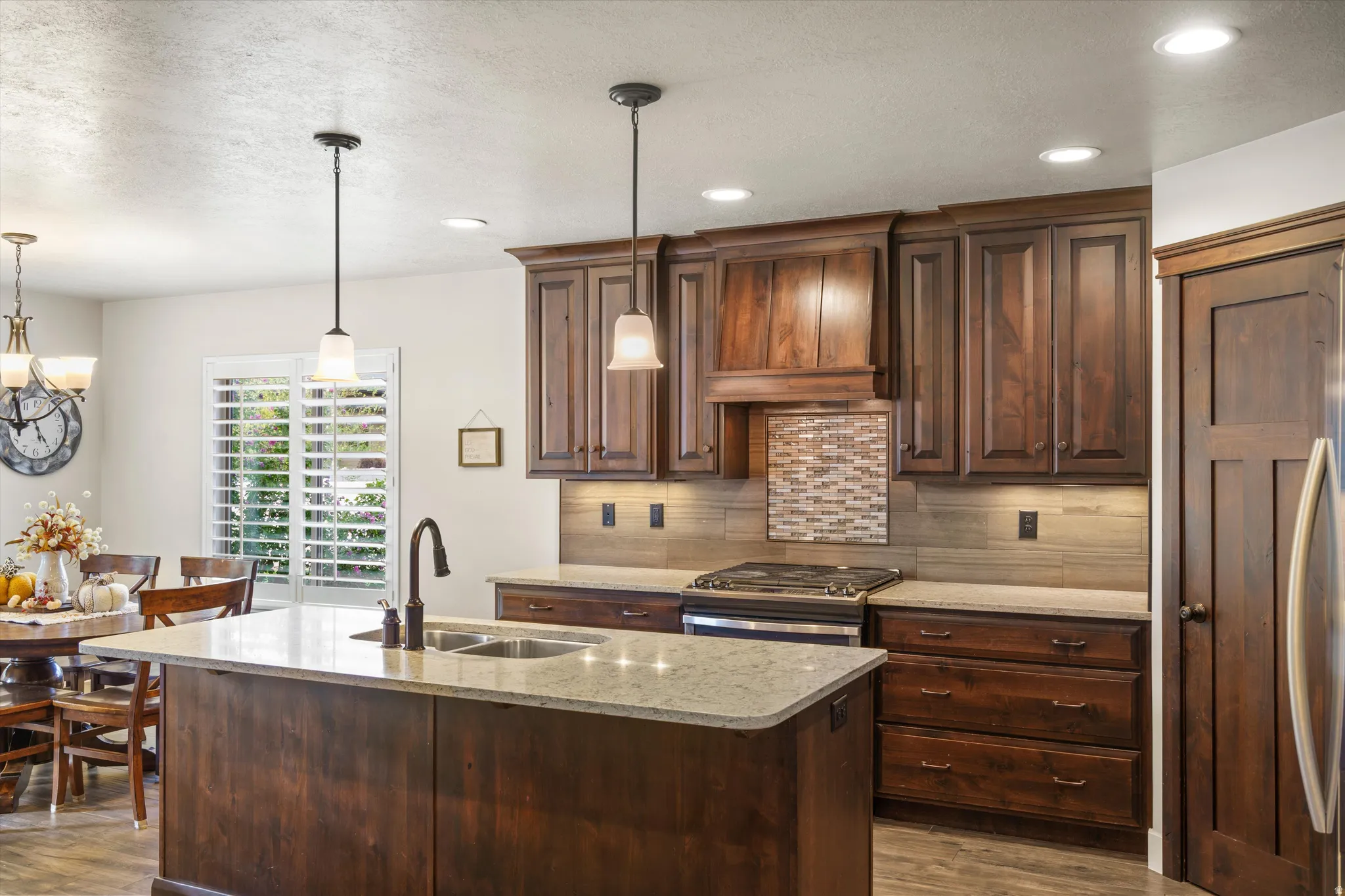 Expansive kitchen island with an undermount double sink, rich wood cabinetry, stainless steel range, and a decorative tile backsplash