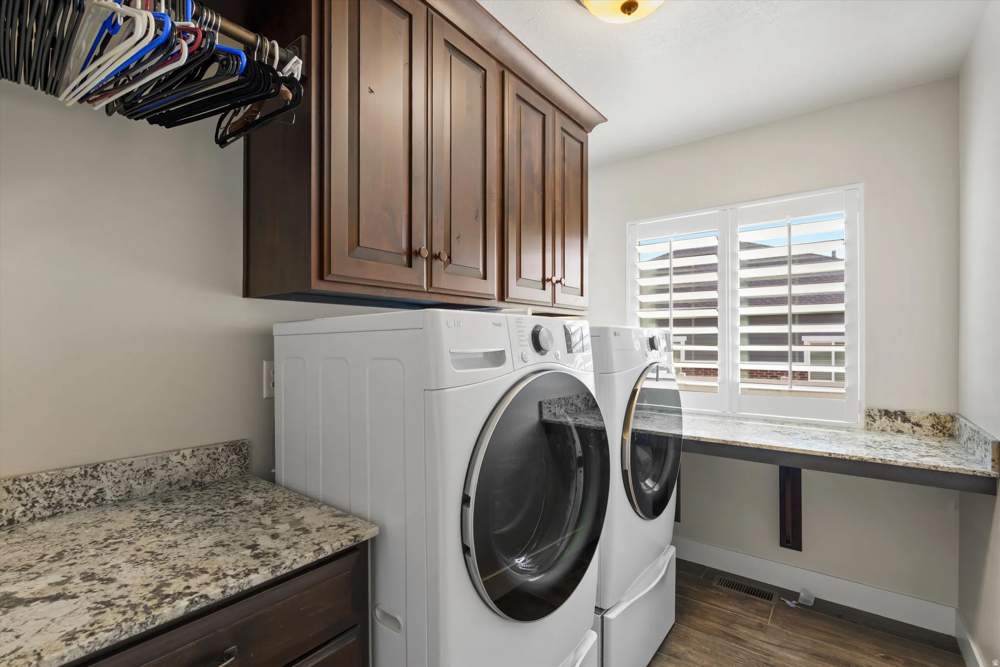 Laundry area featuring wood-finish flooring, ample cabinetry, stone countertops, a window with louvered shutters, and a built-in hanging rod