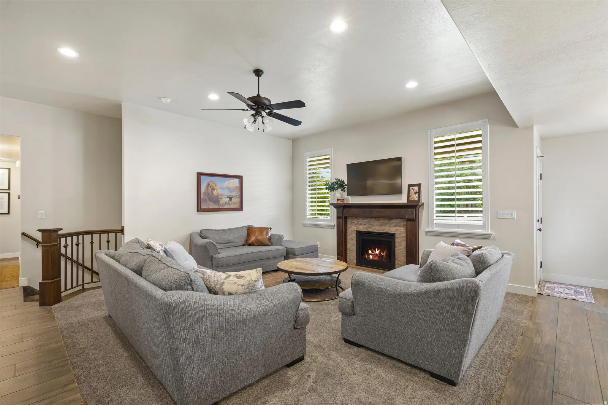 Recessed lighting, wood-finish fireplace surround with tile accent, ceiling fan, plantation shutters, and dark wood railing