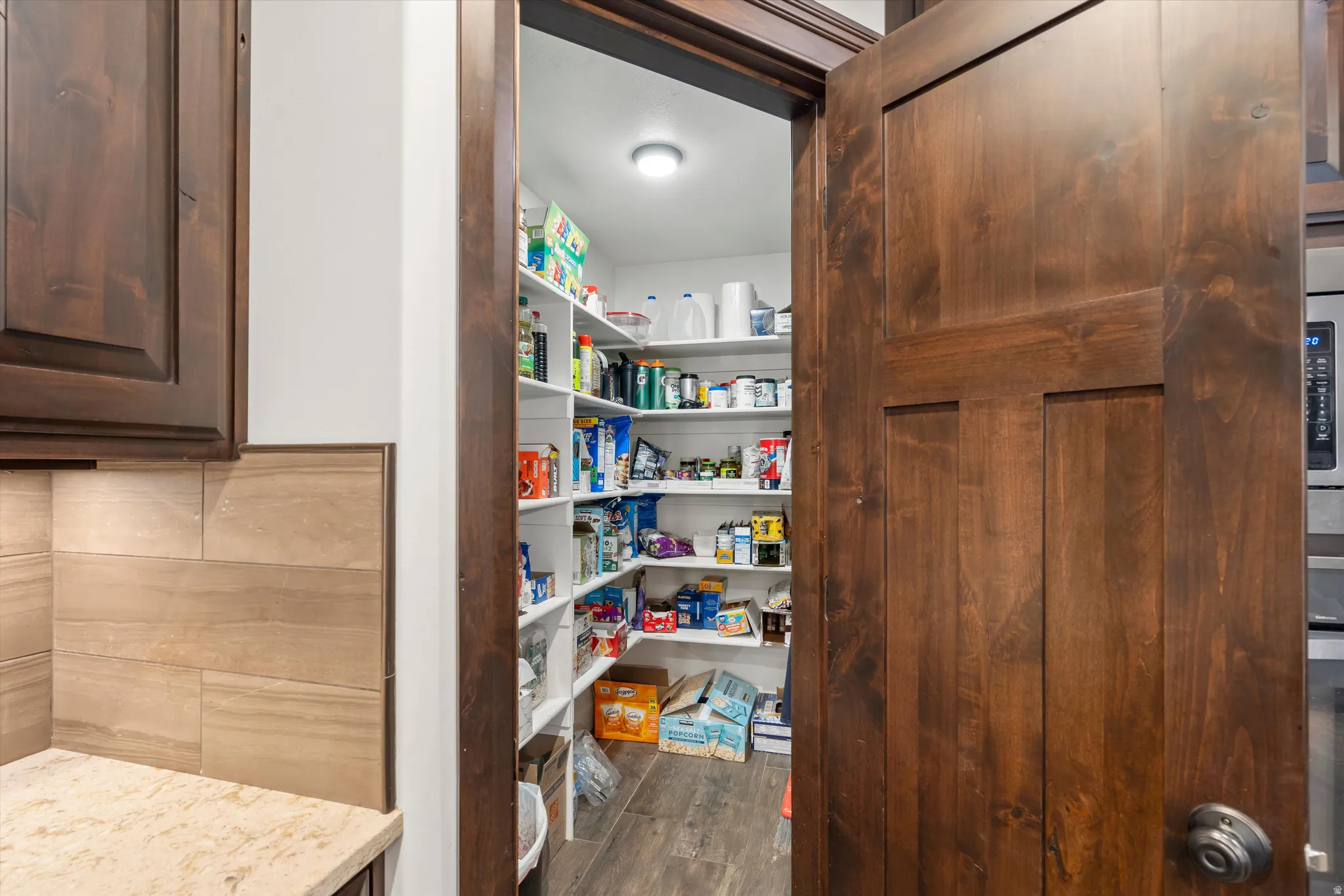 Walk-in pantry with extensive shelving, dark wood-finish door, and integrated overhead lighting