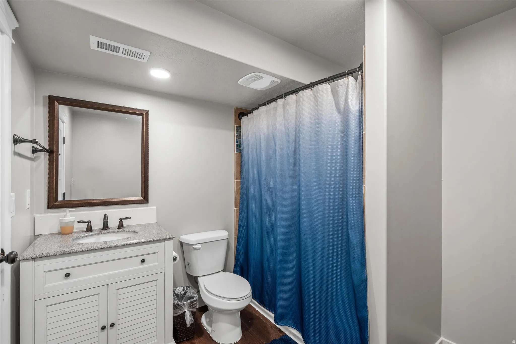 White vanity with louvered cabinet doors, stone countertop, and an undermount sink