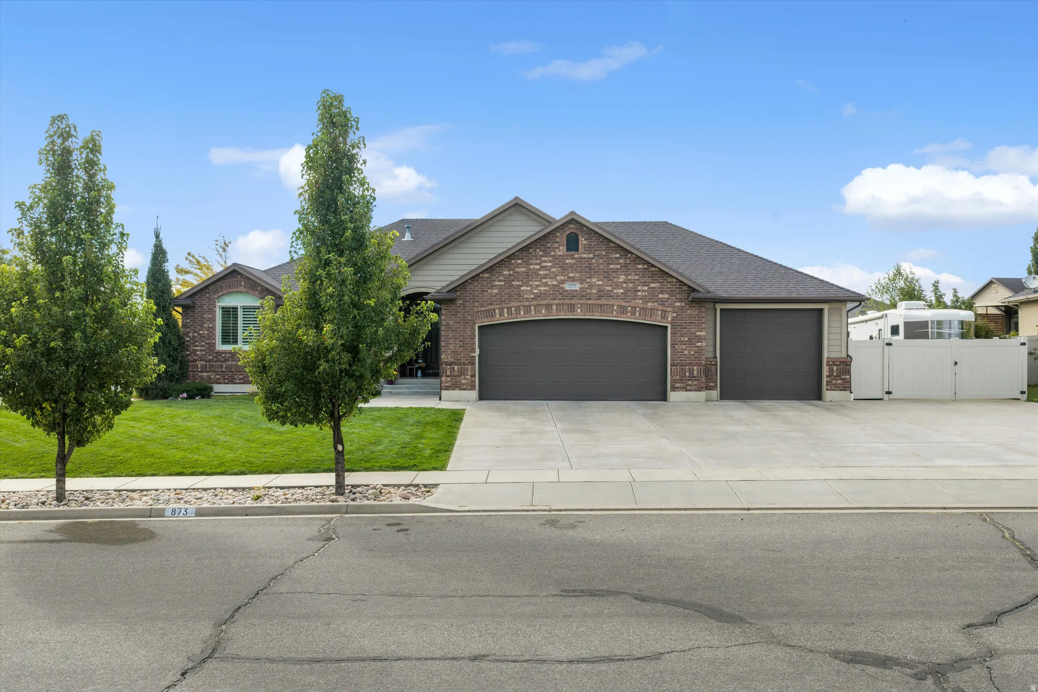 Brick facade with stone accents, mature trees, attached double garage, additional single garage, and a concrete driveway
