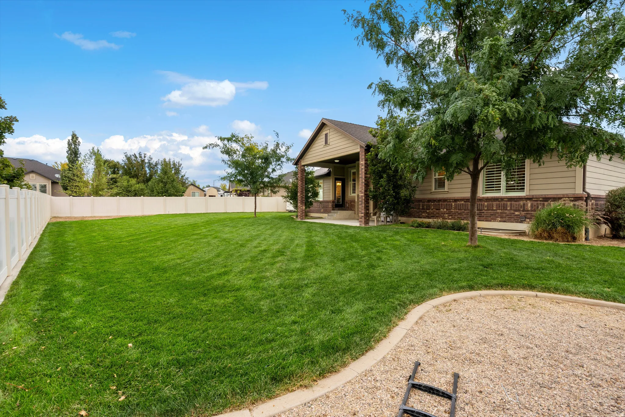 Expansive backyard featuring a manicured lawn, established trees, and a gravel play area