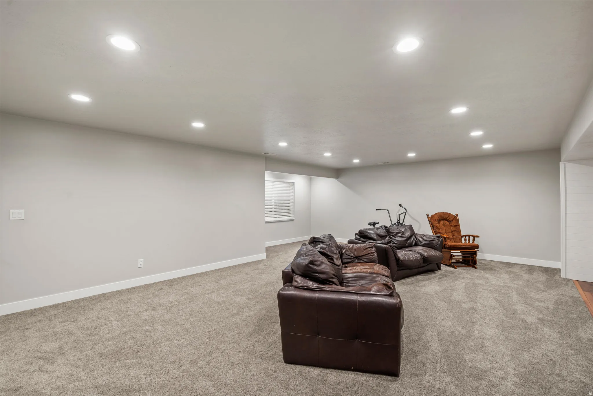Recessed lighting illuminates a carpeted open-concept space with light gray walls