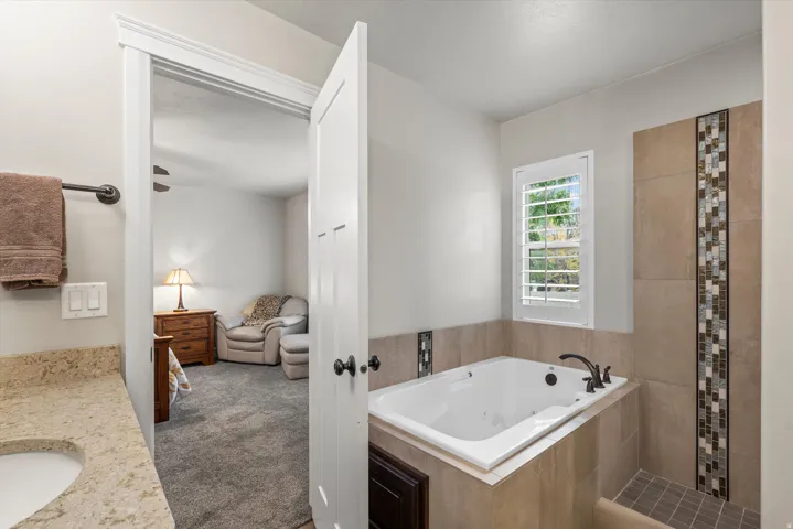 Built-in jetted tub, separate tiled shower with mosaic accent, window with plantation shutters, vanity with stone countertop and undermount sink