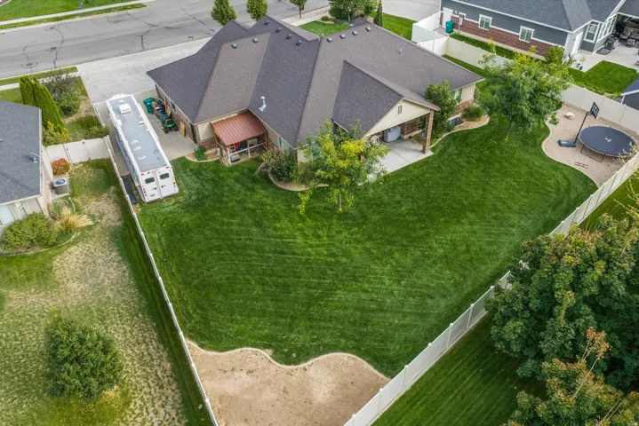 Expansive rear yard featuring a manicured lawn, established trees, covered patio, and perimeter fencing