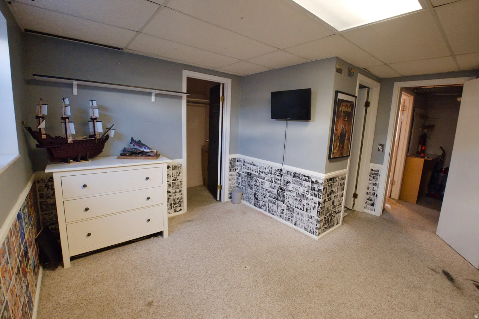 Carpeted room featuring light gray walls, built-in shelving, and a drop ceiling with integrated lighting