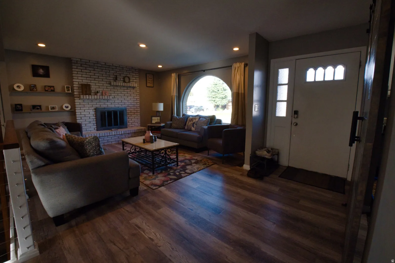 Wood-finish flooring throughout, brick fireplace with mantel, recessed lighting, and an arched window