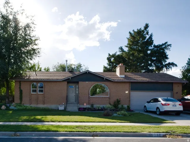 Brick exterior with an attached garage, featuring a well-maintained lawn and mature trees