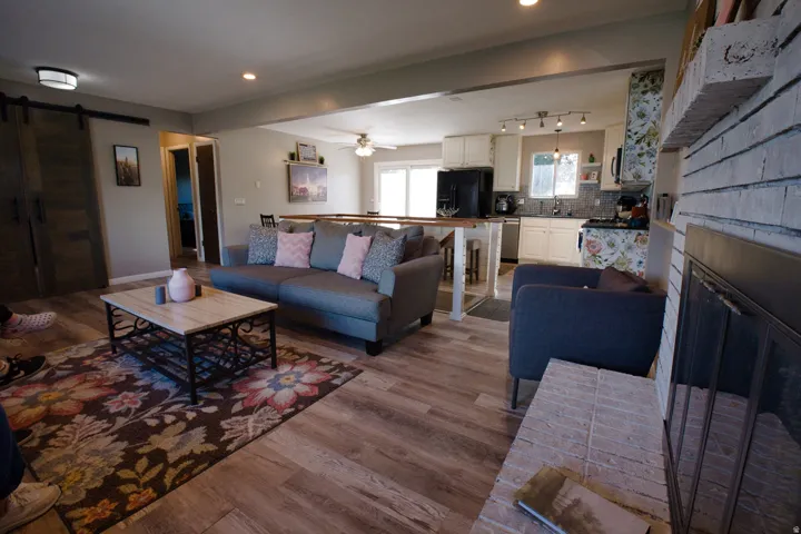 Open-concept living area featuring wood-finish flooring, a painted brick fireplace, and a kitchen with white cabinetry and dark appliances