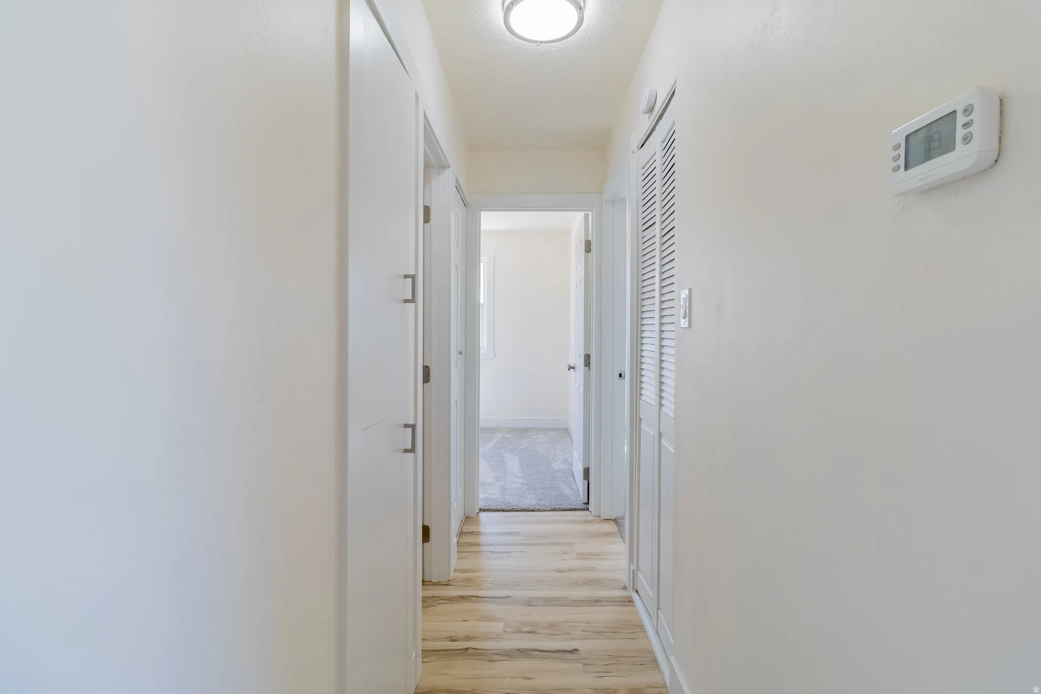 Hallway featuring wood-finish flooring, recessed lighting, white walls, and a digital thermostat