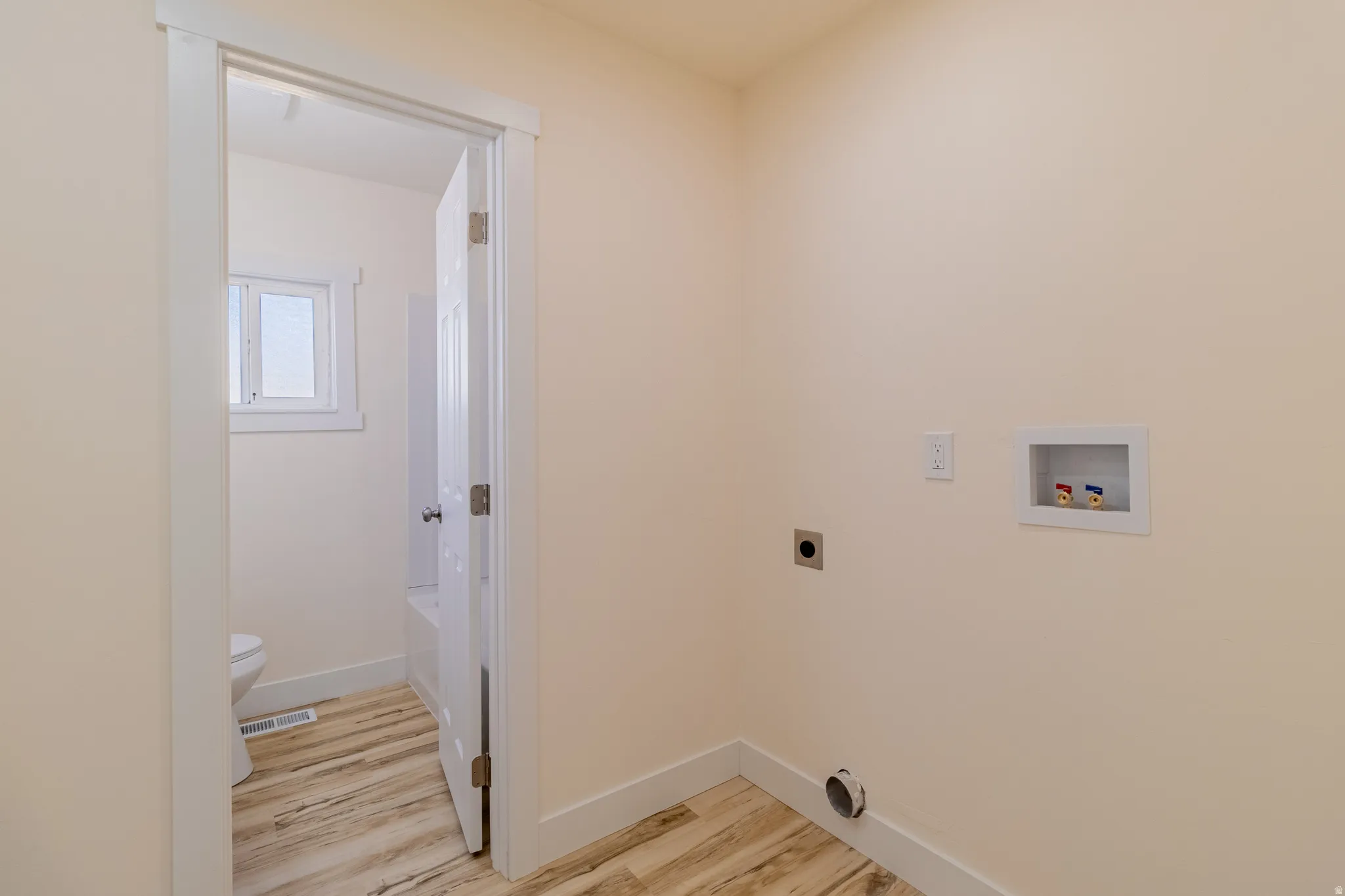 Laundry area with wood-finish flooring and wall-mounted utility connections