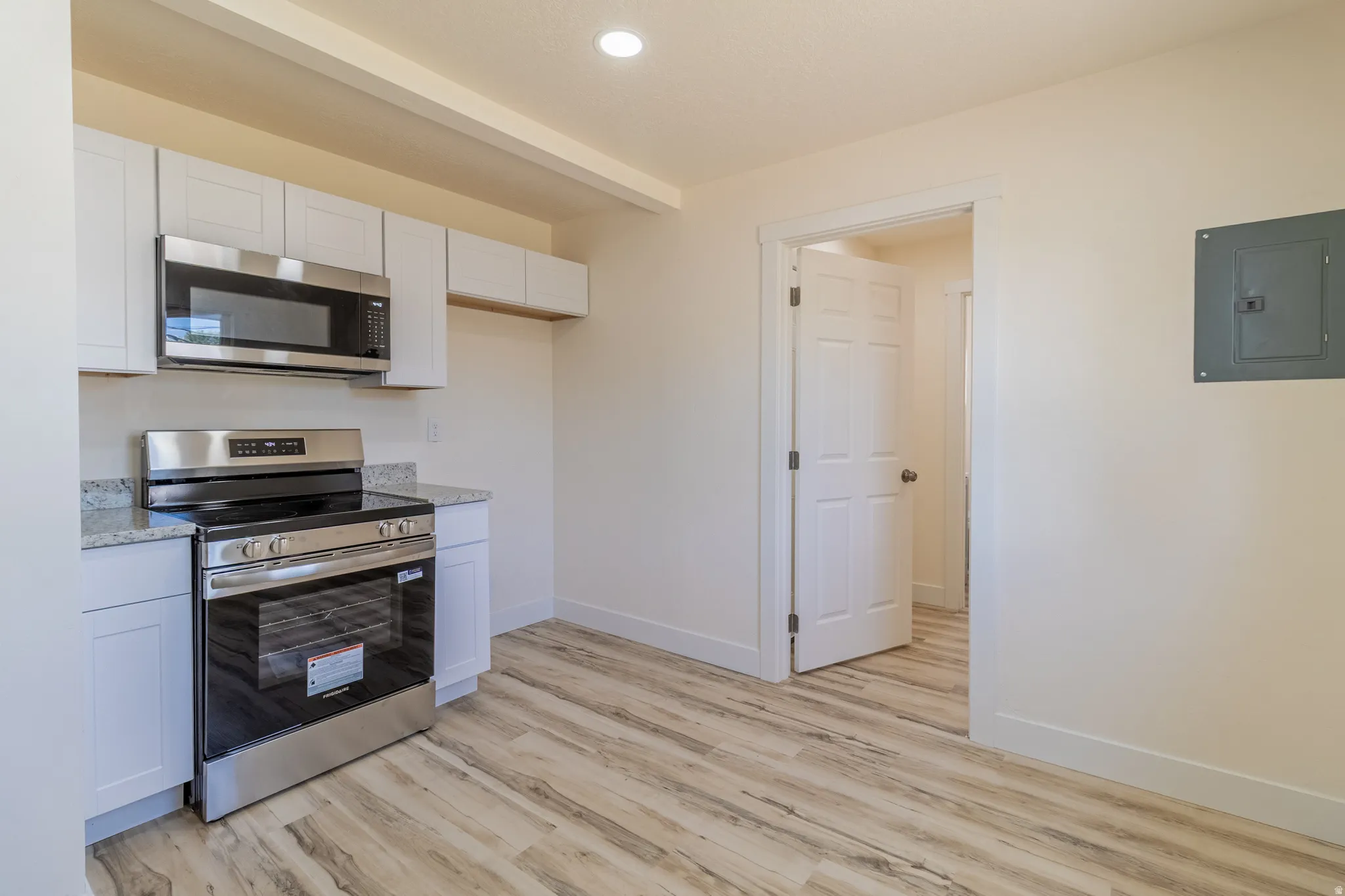 Kitchen featuring wood-finish flooring, white cabinetry, granite countertops, stainless steel electric range, and stainless steel microwave