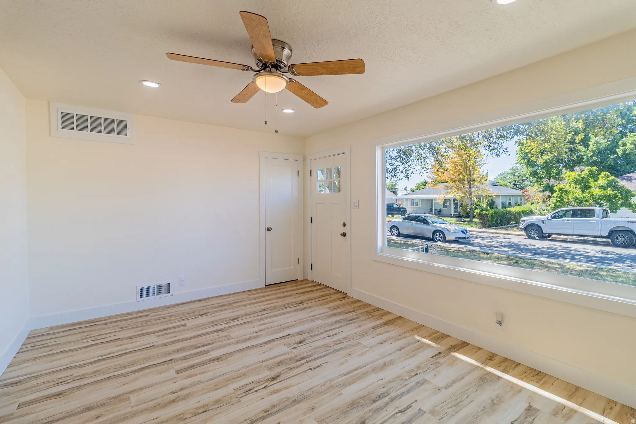 Spacious room featuring light wood-finish flooring, a large picture window, recessed lighting, and a ceiling fan with integrated lighting