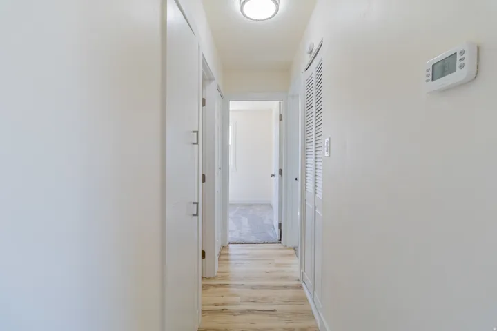 Hallway featuring wood-finish flooring, recessed lighting, white walls, and a digital thermostat