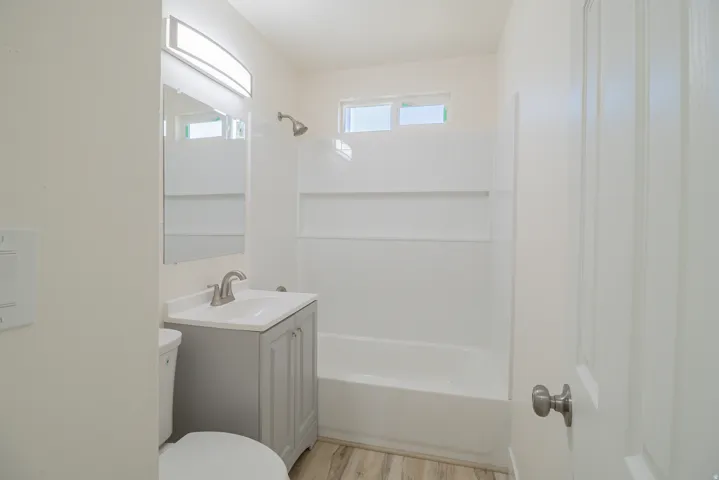 Bathroom featuring a neutral vanity, integrated sink, brushed nickel faucet, wood-finish flooring, and a shower-tub combination