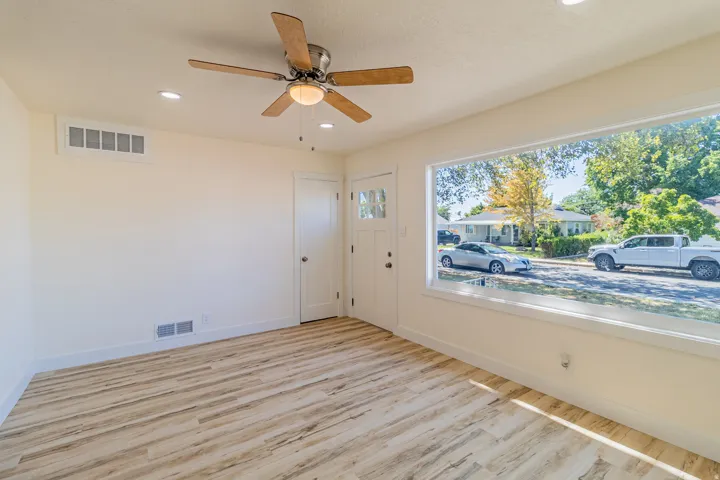 Spacious room featuring light wood-finish flooring, a large picture window, recessed lighting, and a ceiling fan with integrated lighting