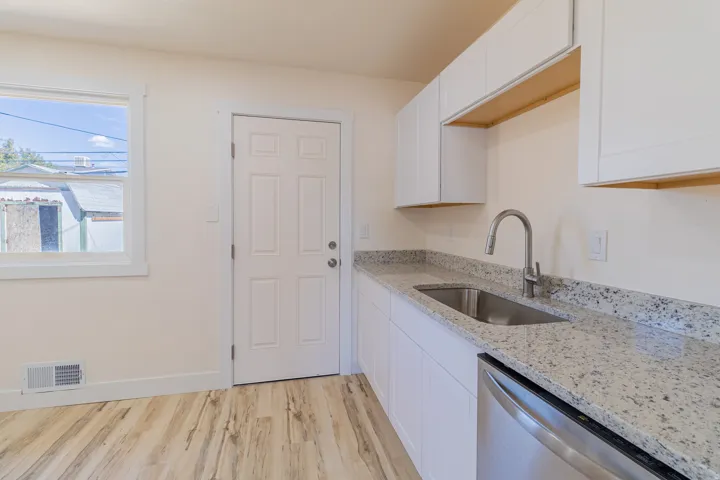 Modern white cabinetry with under-cabinet lighting, stainless steel sink with a high-arc faucet, granite countertops, and wood-finish flooring