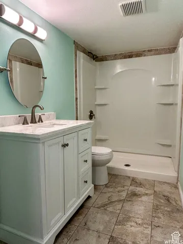 White vanity with a light-colored countertop, an oval mirror, and a full shower enclosure with integrated shelving