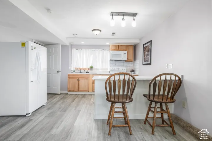 Wood-finish flooring throughout, light wood-tone cabinetry, white subway tile backsplash, white countertops, and recessed lighting