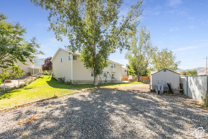 Gravel parking area, side yard with green lawn, white exterior siding, storage shed, and mature trees
