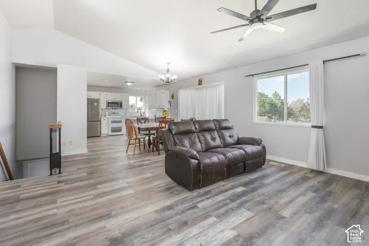 Vaulted ceiling with a ceiling fan, wood-finish flooring, recessed lighting, and a kitchen with white cabinetry