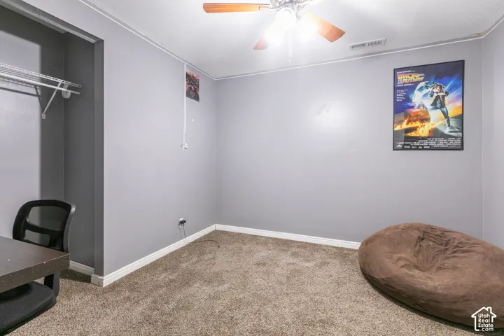 Carpeted room with a ceiling fan light fixture and a built-in closet featuring wire shelving