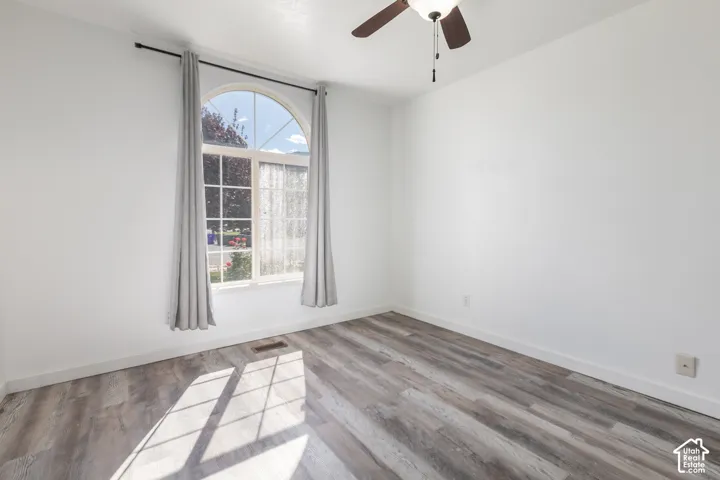 Arched window with gridded panes, wood-finish flooring, ceiling fan, and white painted walls