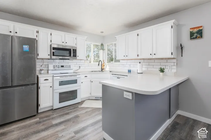 Kitchen featuring white cabinetry, wood-finish flooring, subway tile backsplash, stainless steel appliances, and a peninsula with countertop seating