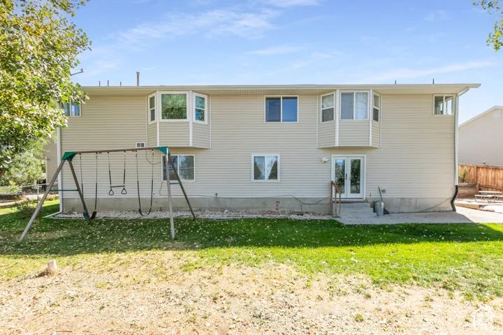 Rear exterior with beige siding, two bay windows, and a ground-level patio