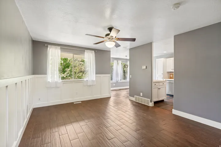 Wood-finish flooring, white wainscoting, ceiling fan with light fixture, and white cabinetry